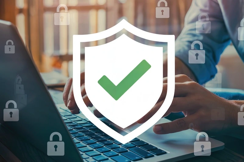 A person types on a laptop with a large shield and green checkmark graphic overlay, symbolizing cybersecurity or data protection. Transparent padlock icons appear across the image, emphasizing security.