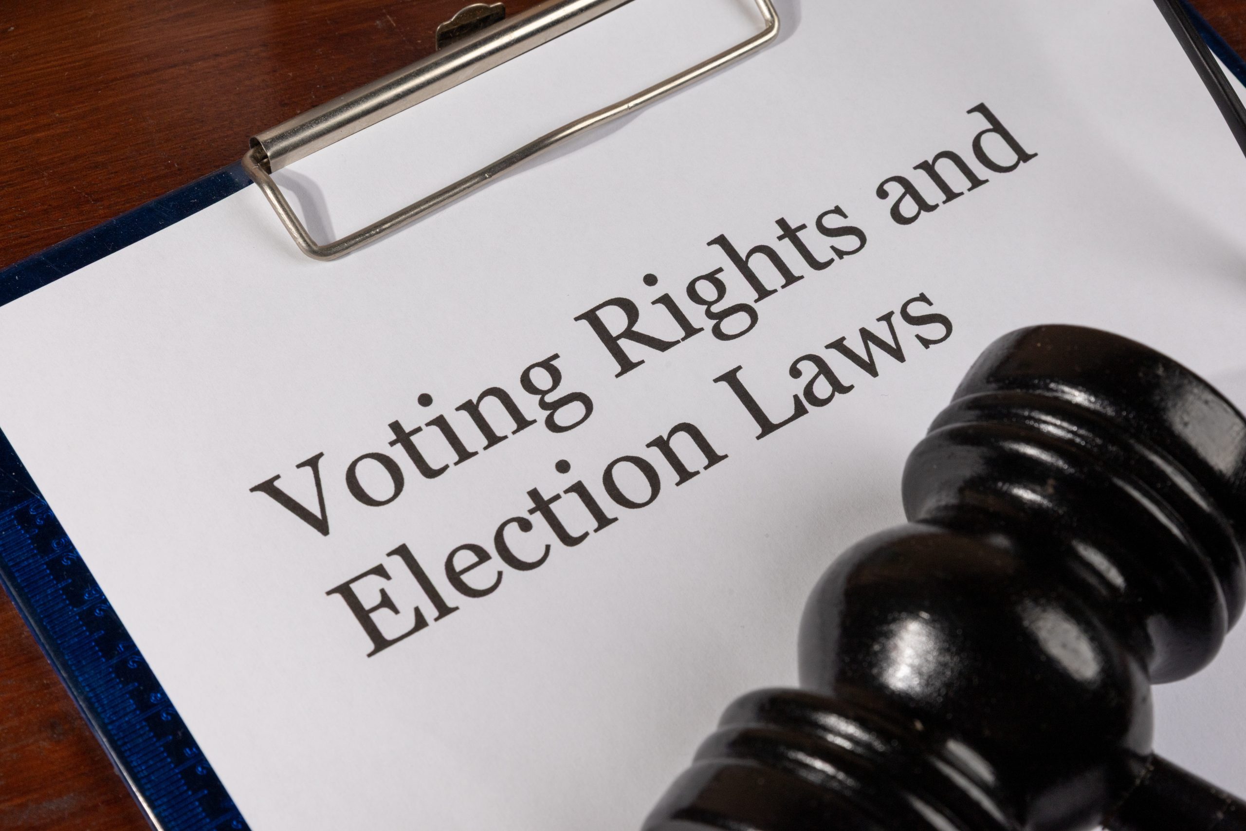 A legal document titled "Voting Rights and Election Laws" is placed neatly on a wooden desk, accompanied by a judge’s gavel, symbolizing authority and legal enforcement. A clipboard holds a document titled "Voting Rights and Election Laws" next to a judge's gavel.