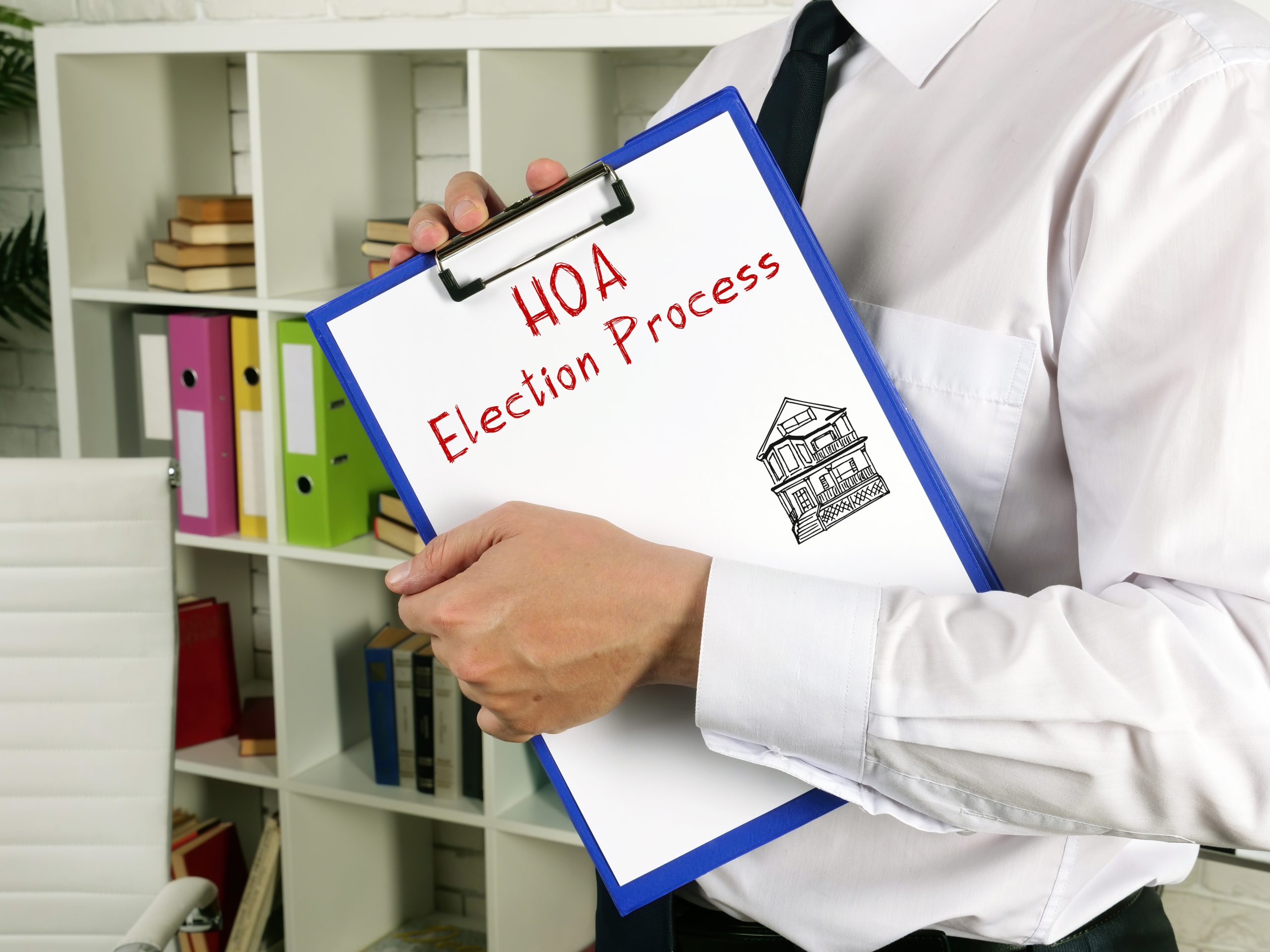 Financial concept meaning Homeowner Association HOA Election Process with inscription on the page. A person in business attire holds a clipboard with a paper titled “HOA Election Process” and a drawing of a house, in an office setting with shelves and folders in the background.